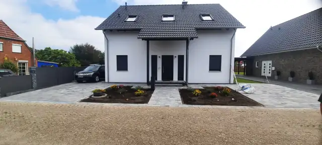 Vorgarten mit Pflaster und Beeten vor einem Neubau